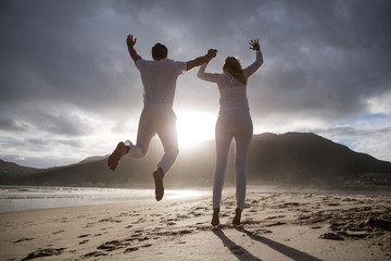 Mature couple jumping in air on the beach