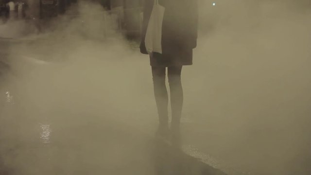 Dismayed young girl enveloped by steam on the night city road