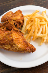 Fried chicken breast with potato chips on a white plate on a wooden table.