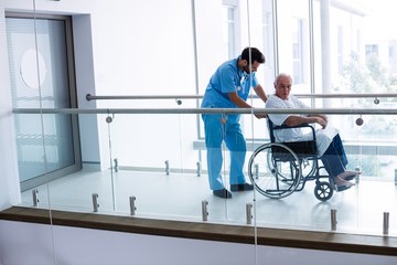Male doctor pushing senior patient on wheelchair in passageway - Powered by Adobe