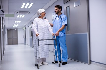 Male doctor assisting senior patient to walk with her walker