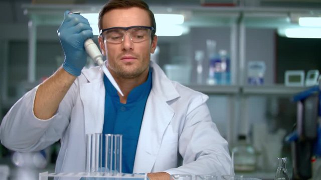 Male scientist conducting research in chemical lab. Scientist working with chemical liquid in research laboratory. Scientist filling test tubes with samples in laboratory. Scientist working in lab