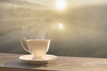 Morning cup of coffee with mist over lake  at sunrise