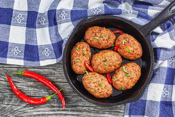 meat cutlets in iron frying pan sprinkled with chili pieces