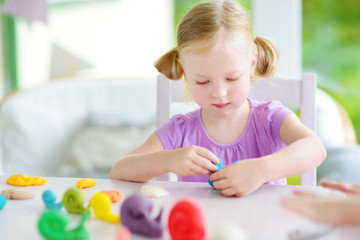 Cute little girl having fun with modeling clay at a daycare. Creative kid molding at home.