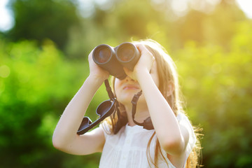 Funny little girl looking through binoculars on summer day