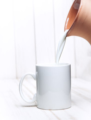 Milk is poured into a cup of pitcher on white background wooden