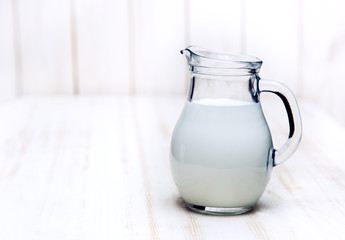 Milk in glass pitcher on white background wooden table