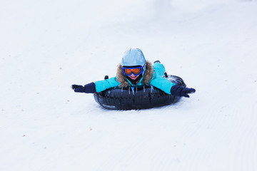 cheerful girl in a helmet and glasses riding on a sled with high mountains
