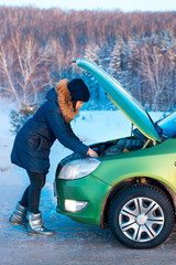 A woman waits for assistance near her car broken down on the road side.