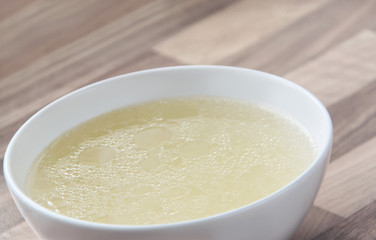 Rich chicken broth in a white bowl on wooden background. Meat chicken bouillon.