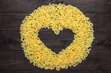 Raw macaroni - pasta Galetti.  In the middle of the empty space in the shape of a heart on a dark wooden background.