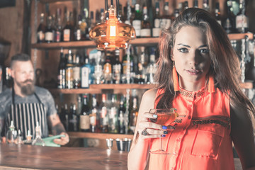 Beautiful girl is drinking a cocktail with ice vapor in the bar