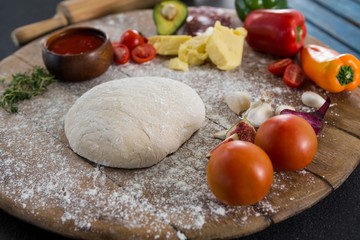 Various ingredients with pizza dough and flour on rolling board