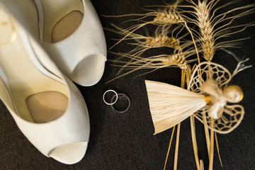 Wedding decoration details. Silver wedding rings and elegant bridal shoes on a grey background and handmade angel of straw