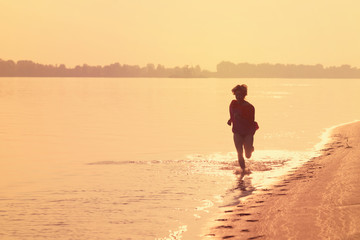Naklejka premium Teen girl running on the water at sunset