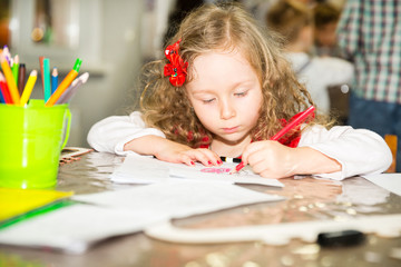 Adorable child girl drawing with colorful pencils in nursery room. Kid in kindergarten in Montessori preschool class.