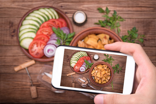 Hands taking photo meat stewed with potatoes in bowl with smartphone.