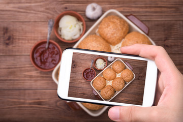Hands taking photo chicken cheese sliders with smartphone.
