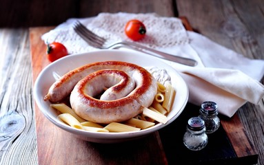 Home fried sausage with boiled pasta in olive oil on old wooden background.