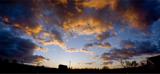 Burning sunset sky panorama with gathering orange clouds and blue sky