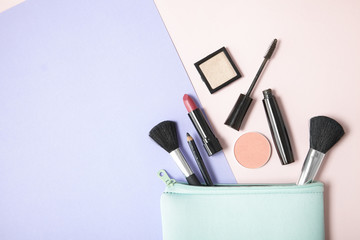 Make up products spilling out of a pastel blue cosmetics bag, on a pink and purple background with...