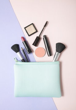 Fototapeta Aerial view of make up products spilling out of a pastel blue cosmetics bag, on a pink and purple background