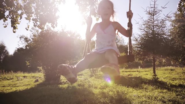 Cute little beautiful girl having fun on swing in a tree swing and smile at the park on sunset