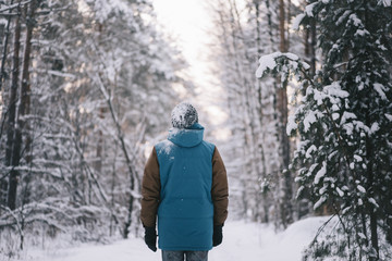 Young man standing all alone in the winter snowy forest