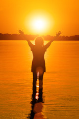 Woman is holding sun  in water at sunset