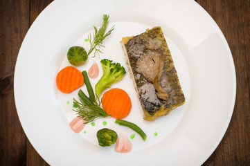 Tasty baked fish on plate on table close-up. Wooden background. Top view. Close-up