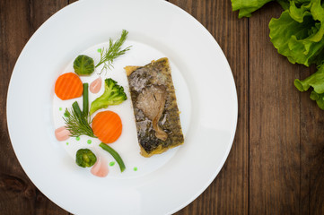 Tasty baked fish on plate on table close-up. Wooden background. Top view. Close-up