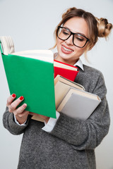 Cheerful cute young woman in glasses holding and reading books