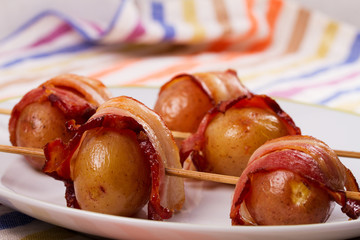 Bacon wrapped potato on skewers on white plate