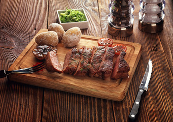 Roasted pork steak cut into slices on a wooden stand.