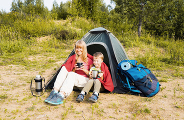 Happy  mother and son camping in tent and drinking tea on the nature.