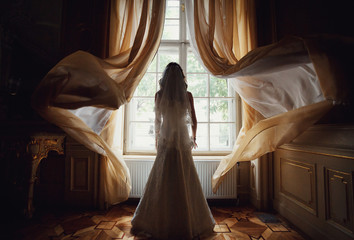 The charming bride stands near window in the restaurant