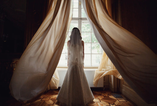 The charming bride stands near window in the restaurant