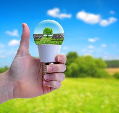 Hand with thumb up holding a eco LED bulb with solar panel.  The concept of sustainable resources.