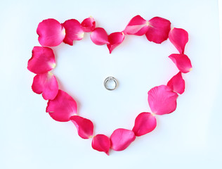 Petals of rose flower in heart shape with couple wedding rings isolated on white background.