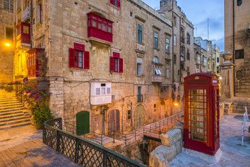 Fototapeta na wymiar Valletta, Malta - Red vintage british telephone box and footbridge and traditional red balconies in the ancient city of Valletta early in the morning