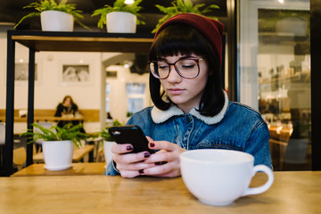 young girl hipster use the phone and drinking a hot drink in a nice cafe