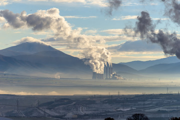 Power plant with smoking chimneys. Mountains in the background.. - 136311261