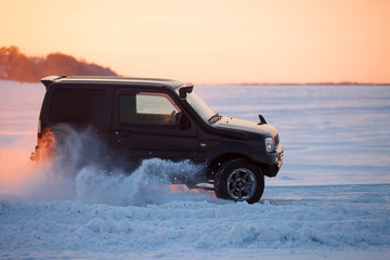 Suzuki Jimny moving on ice of a frosn river at sunset