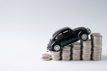 A toy black car model in top of stack of coins isolated on white background with copy...