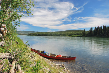 Tied up and abandoned red canoe lying on the river bank of the Yukon River in Canada