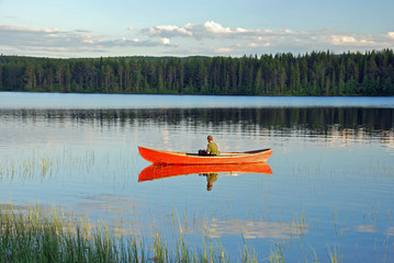 Man sitting in a red canoe on a lake in Finland and fishing at sunset