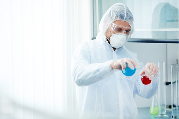 Fototapeta na wymiar Researcher in protective clothes mixing two liquid substances in lab
