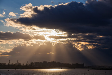 Sunset on the river. Sunset over the city. Sun rays through the clouds. River in the city. 