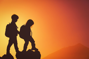 Silhouettes of little boy and girl hiking at sunset